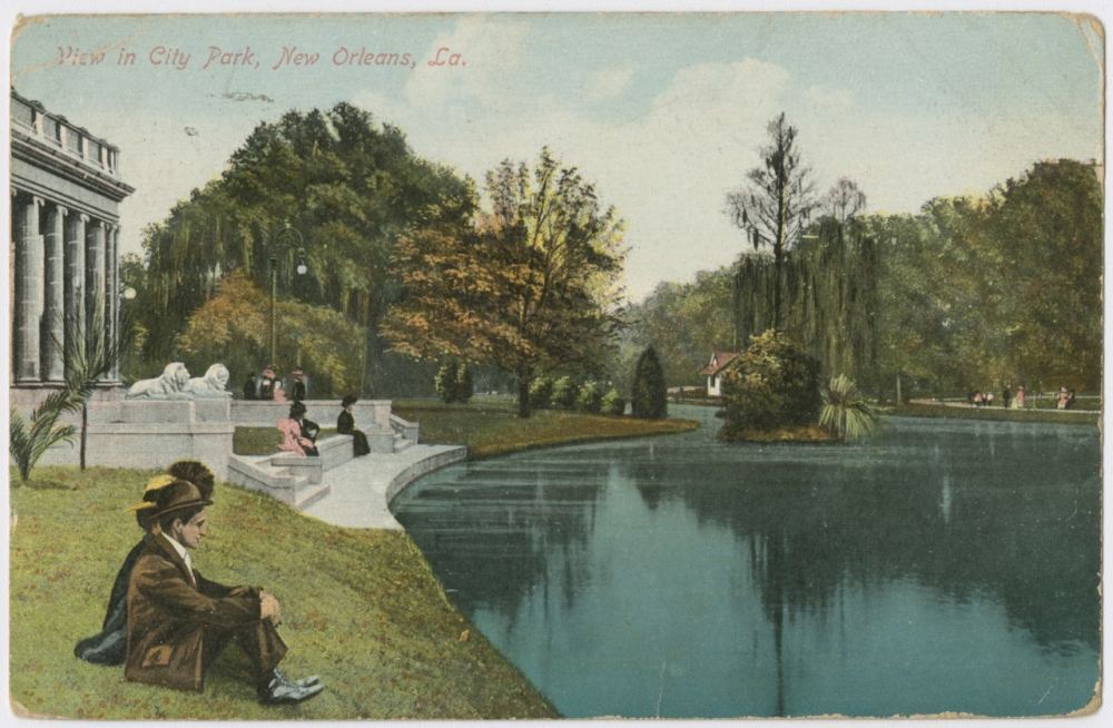 A circa 1908 postcard reproduced from a photograph showing people sitting on the lawn between the Peristyle and the lagoon in City Park.