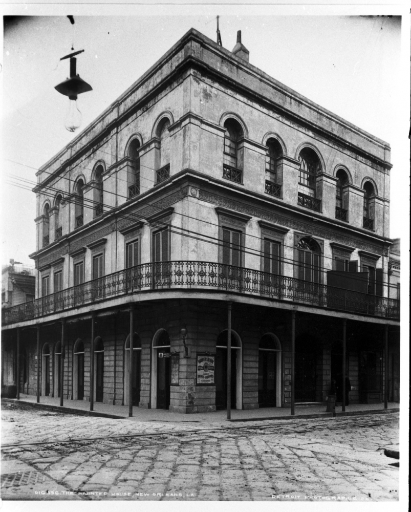 Black-and-white photo of a three-story building with a wrought iron balcony.