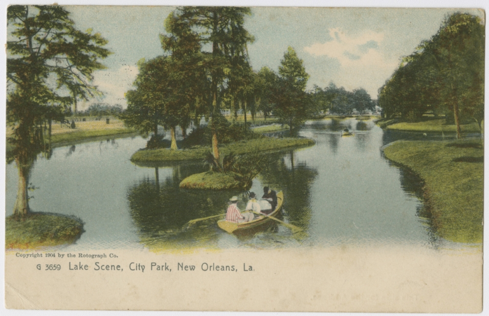 A 1904 postcard made from a photograph, labeled "Lake Scene, City Park, New Orleans, La." In the foreground is a rowboat with three passengers. Three small islands are in the center of the lake, all of them with trees, bushes, or palmettos. A second boat with a single passenger is in the background. The lake is rimmed with many more trees. 