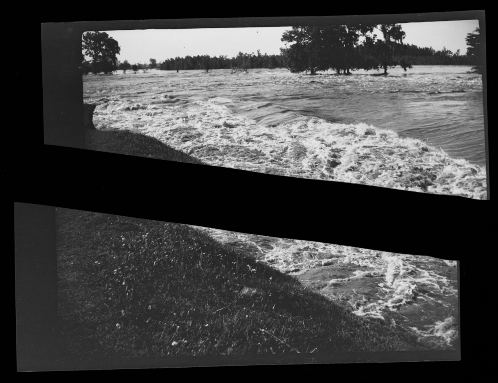 Black and white photo of flood waters at shore line. The photo is ripped.