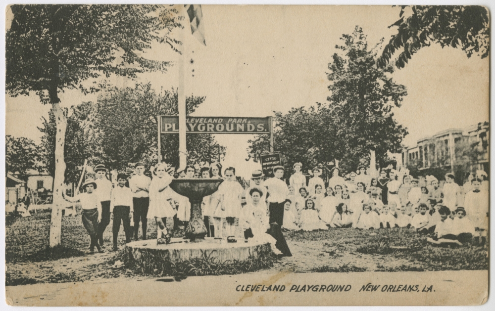 A circa 1919 black-and-white postcard features a group of about 50 children and several adults in front of an arched sign reading "Cleveland Park Playgrounds." A partially visible banner in the background reads, "Civic Improvement and Playground Association." The boys all wear dark knickers and white oxford shirts; most wear hats. The girls all wear white dresses. Because New Orleans playgrounds were segregated, all the people in the photo are white. 