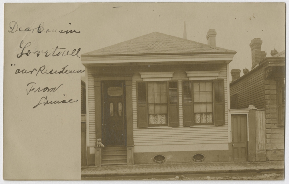A 1907 postcard features the front facade of a single-story, three-bay residence located in the French Quarter. A small white dog sits on the steps leading to the front door. 