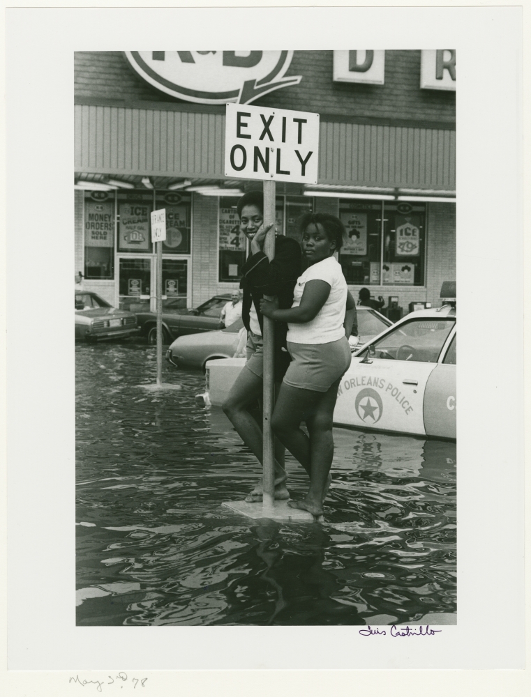 A woman and child hold onto an "exit only" sign, surrounded by water, in the flooded parking lot of a K&B drugstore