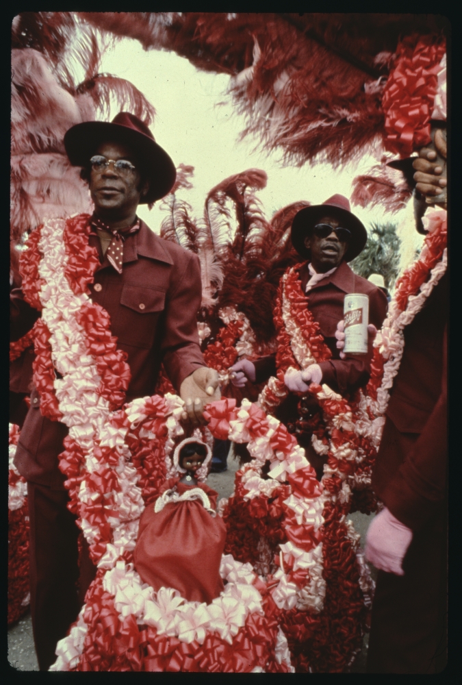 Monk Boudreaux of the Golden Eagles Mardi Gras Indians, wearing all deep red shirt, is seen holding a large decoration covered in red-and-white bows at Jazz Fest. 