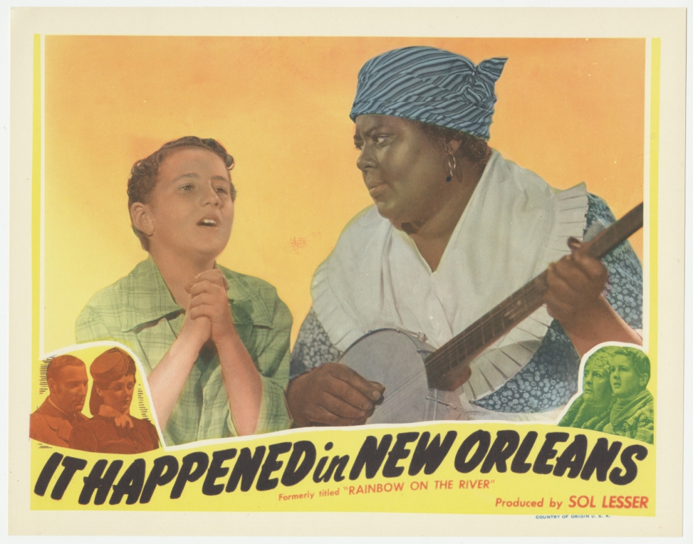 A colorized lobby card with a yellow border. In the center, a young white boy in a green shirt sings and a Black woman in a blue dress with a large white collar and a blue headdress holds a banjo.