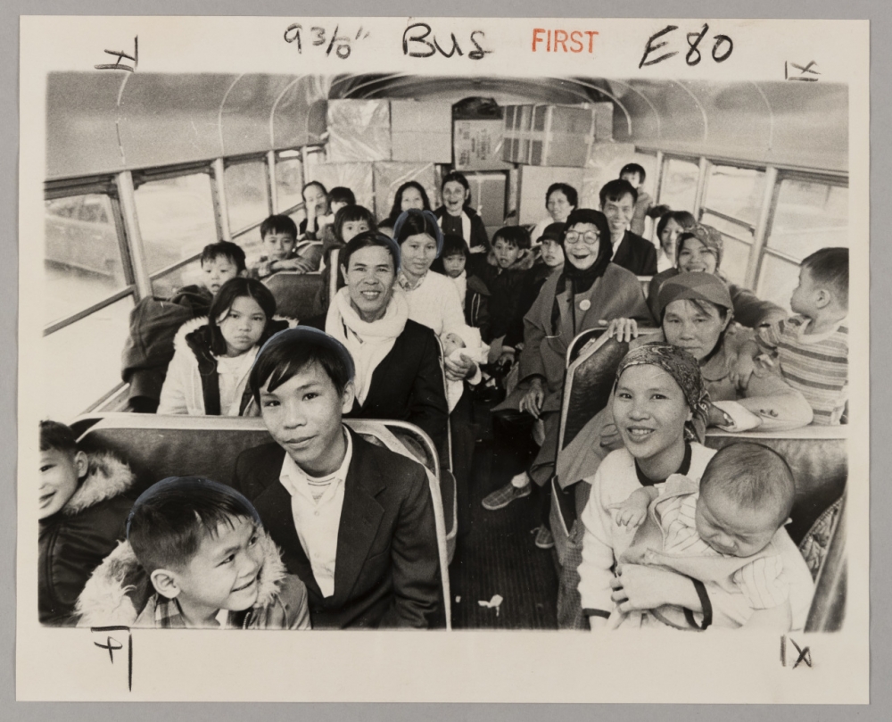 Black and white photograph featuring smiling Vietnamese immigrants on a bus.