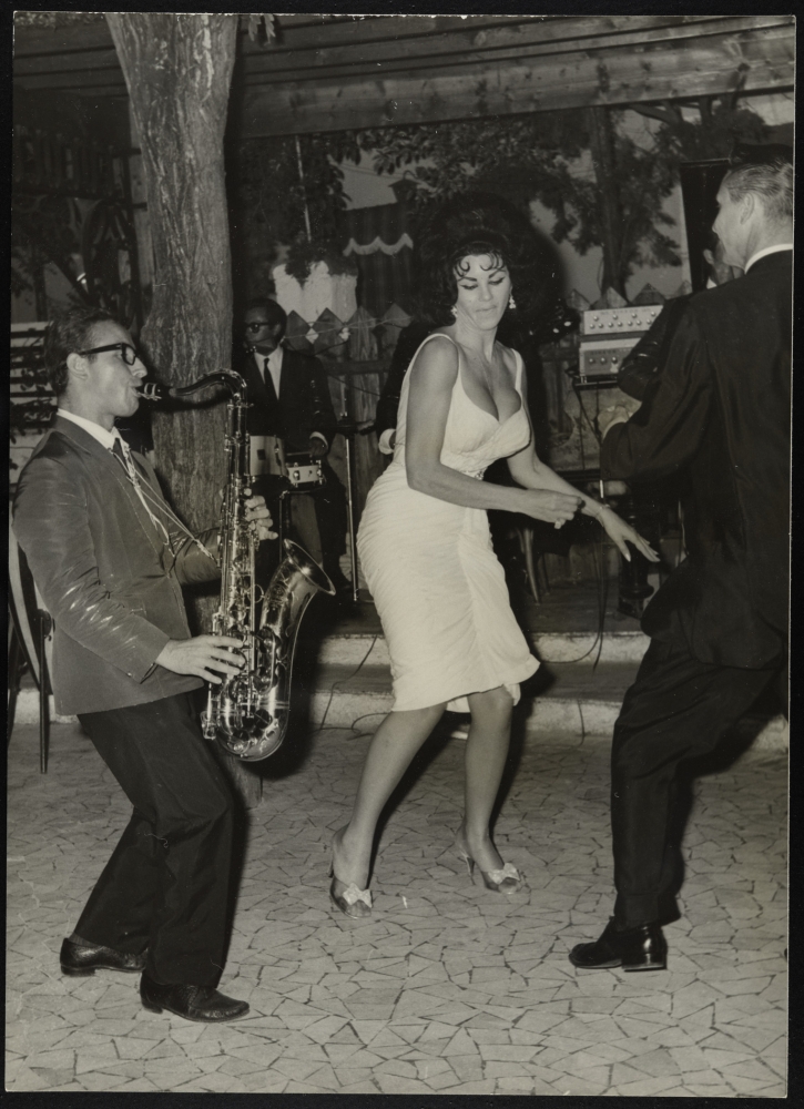 Black-and-white photograph of a dark-haired woman in a white dress dancing.