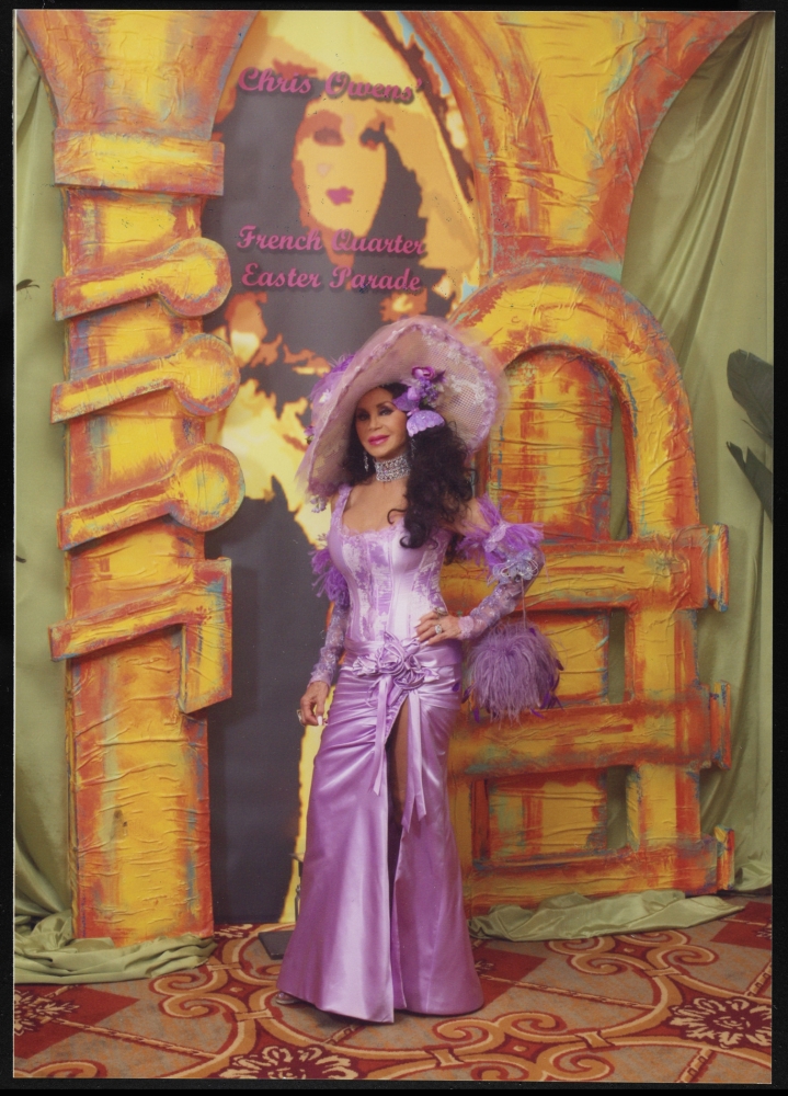 Photograph of a dark-haired woman wearing an elaborate, floor-length lavender dress and matching hat.