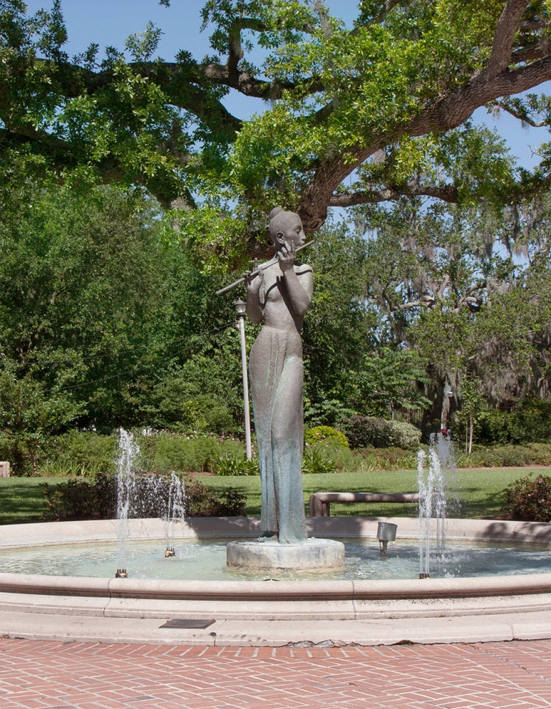 A photo of one of Alférez’s statues in City Park. The statue is in a fountain, and depicts a woman in a long dress playing a flute.