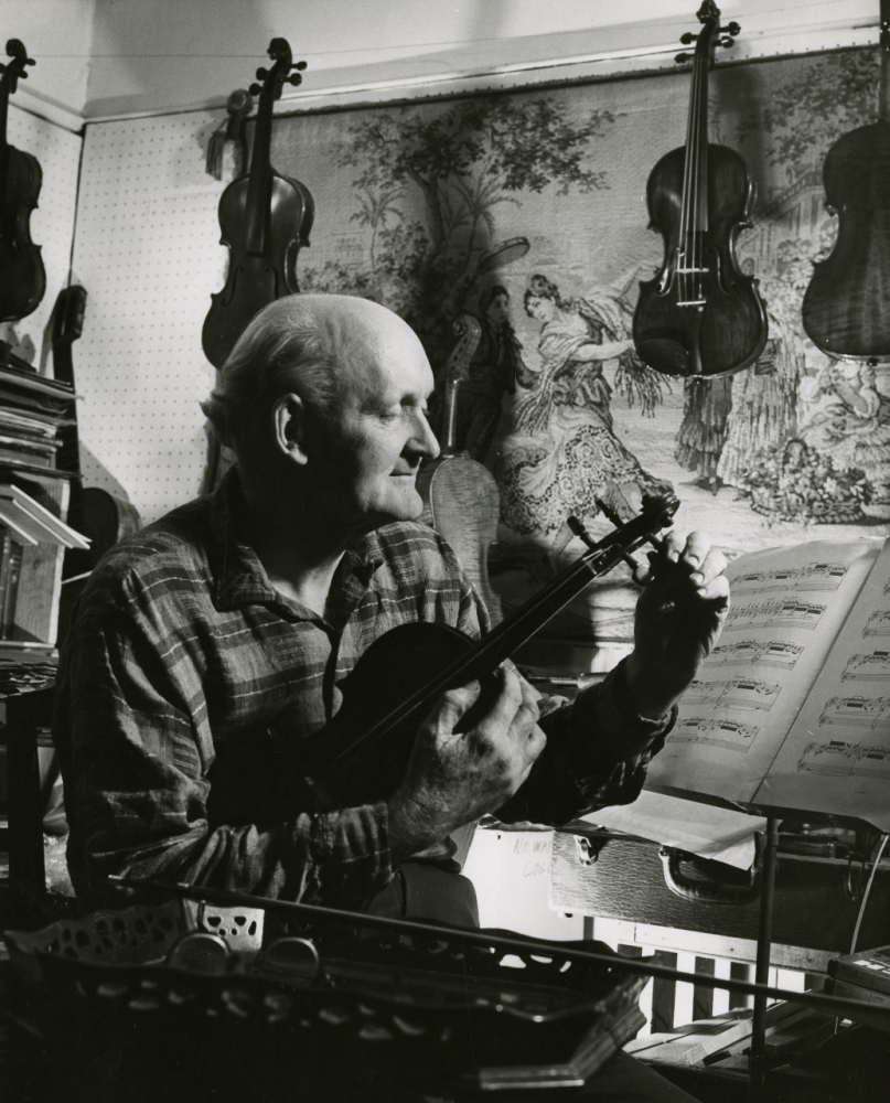 A black-and-white portrait of Bill Russell tuning a violin.
