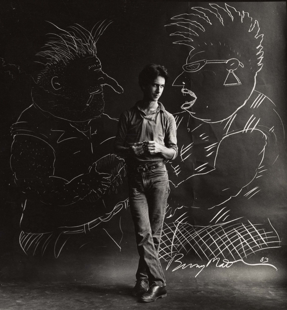 A black-and-white photo of Bunny Matthews standing between drawings of his cartoon characters Vic and Nat'ly