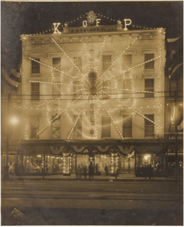 Black-and-white photograph of a three-story building decorated with white lightbulbs in the shape of a spiderweb.