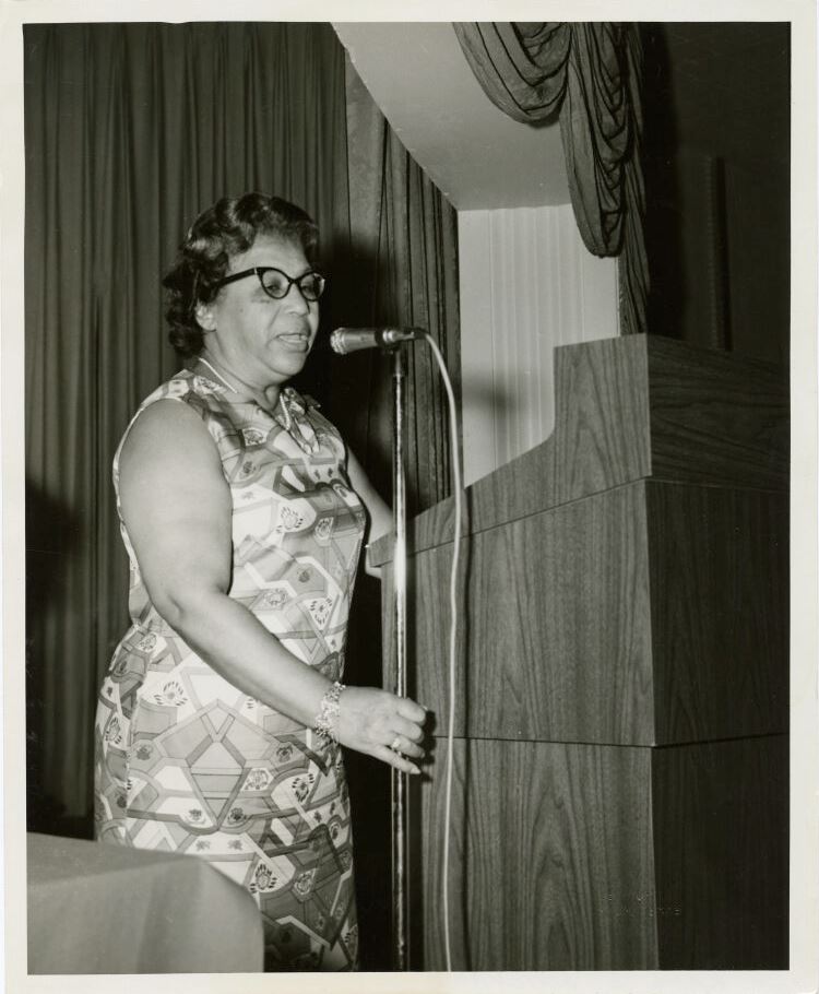 A woman stands and speaks into a microphone at a podium.