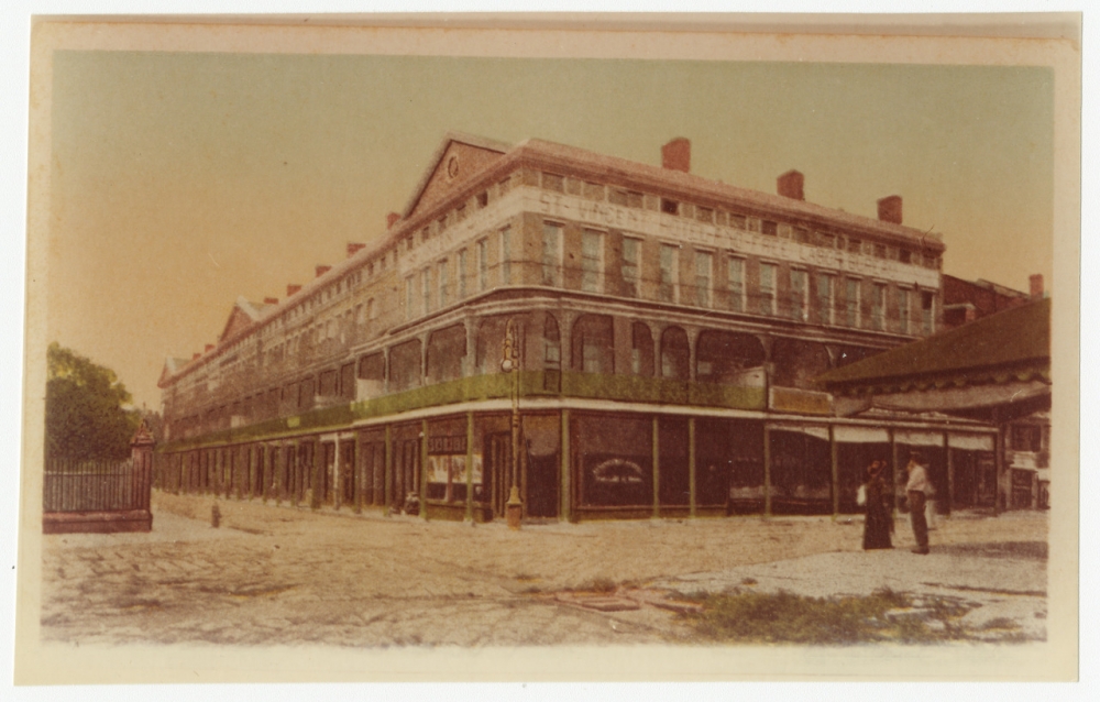 Colorized photograph of a large multi-story apartment building with wrought iron balconies on the second story.