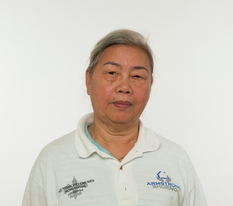 Photo of a middle-aged Vietnamese woman with gray hair looking at the camera. She wears a white polo shirt.