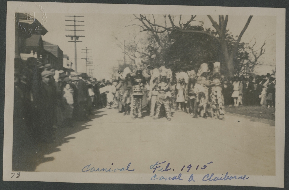 A 1915 black-and-white photograph by George Ernst Durr (1888-1857) showing a large group of Mardi Gras Indians at the corner of Canal and Claiborne Streets in New Orleans. The image is part of a scrapbook.