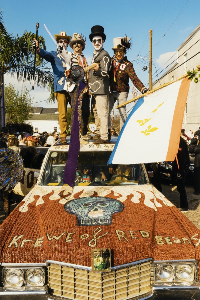 Four white, costumed men from the Krewe of Dead Beans, a sub-krewe of the Krewe of Red Beans, stand on the roof of a vintage in this circa 2015 image from Ryan Hodgson-Rigsbee. The men are wearing costumes made with dried beans, and the car is covered in beans as well.