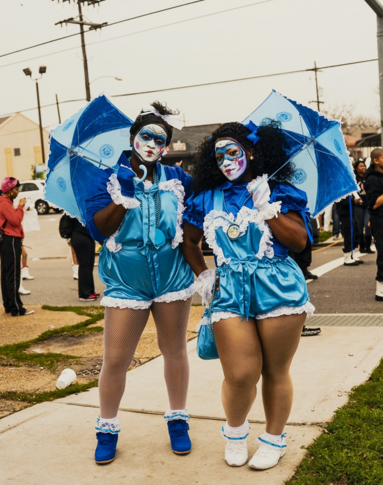 2013 full color image by Ryan Hodgson-Rigsbee of two Black women dressed a New Orleans Baby Dolls, a parading tradition that dates back to the early 1900s and was revived in the 21st century. Their faces are painted to look like dolls and their ruffled blue and white outfits and parasols are styled after the clothes made for dolls.